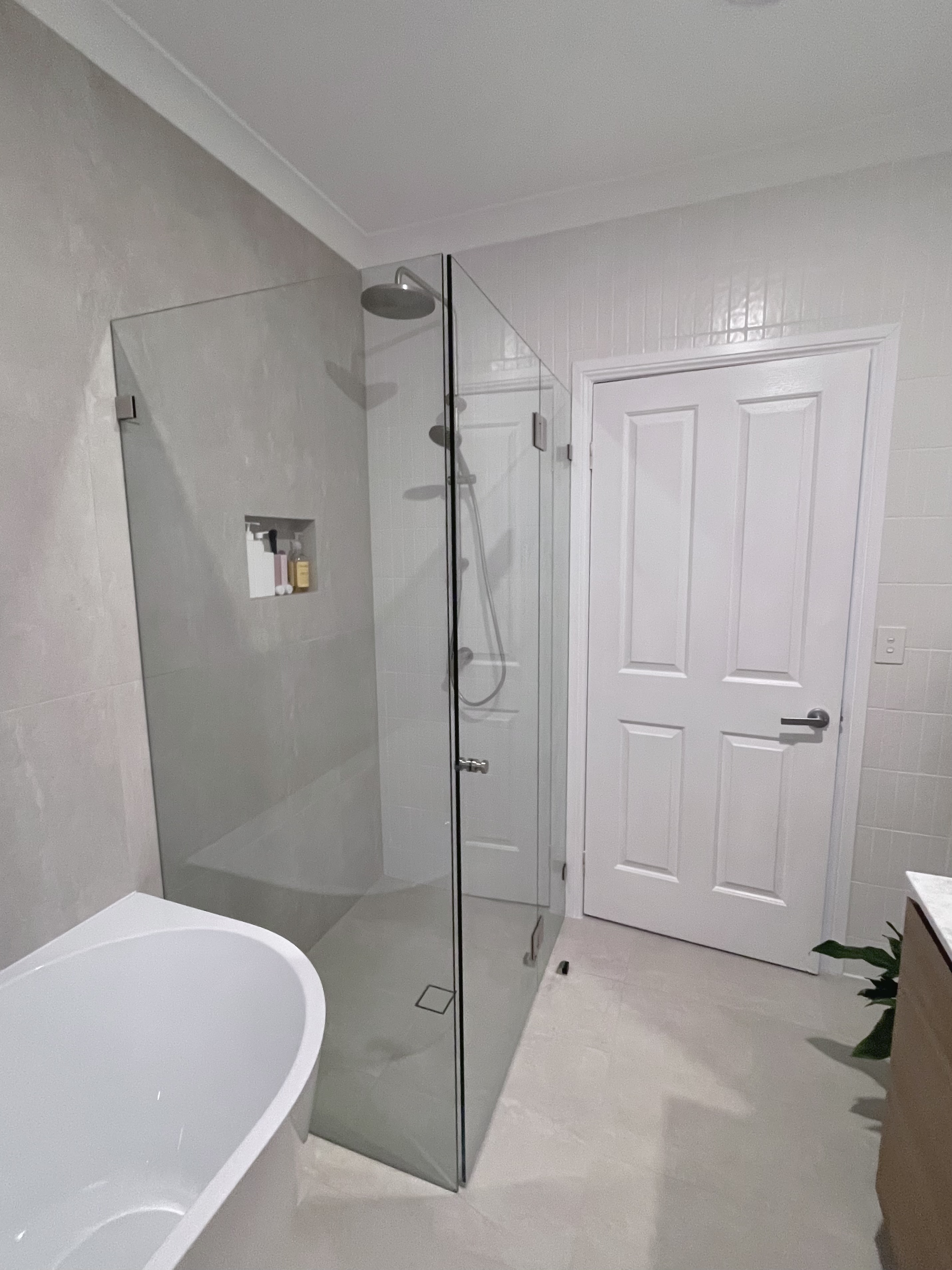 Completed white tile bathroom with bath, shower and wood vanity