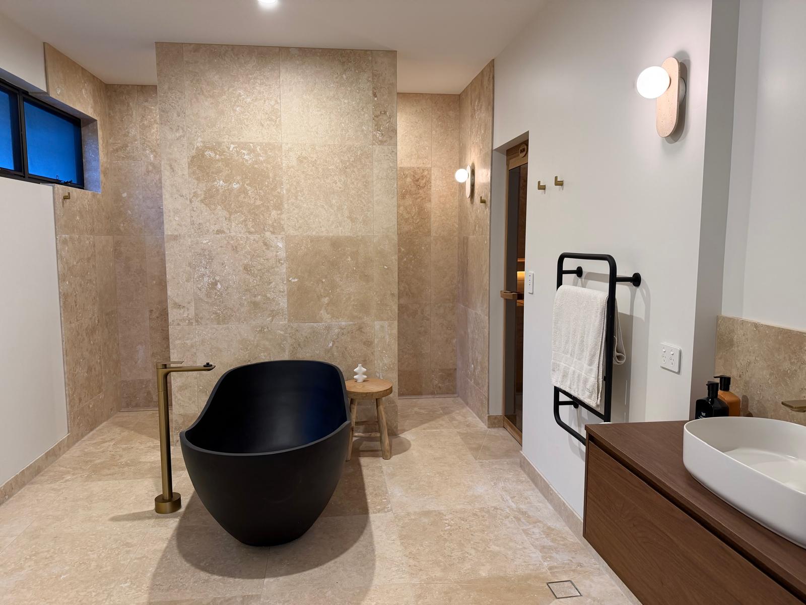 Completed travertine main bathroom with black freestanding bath