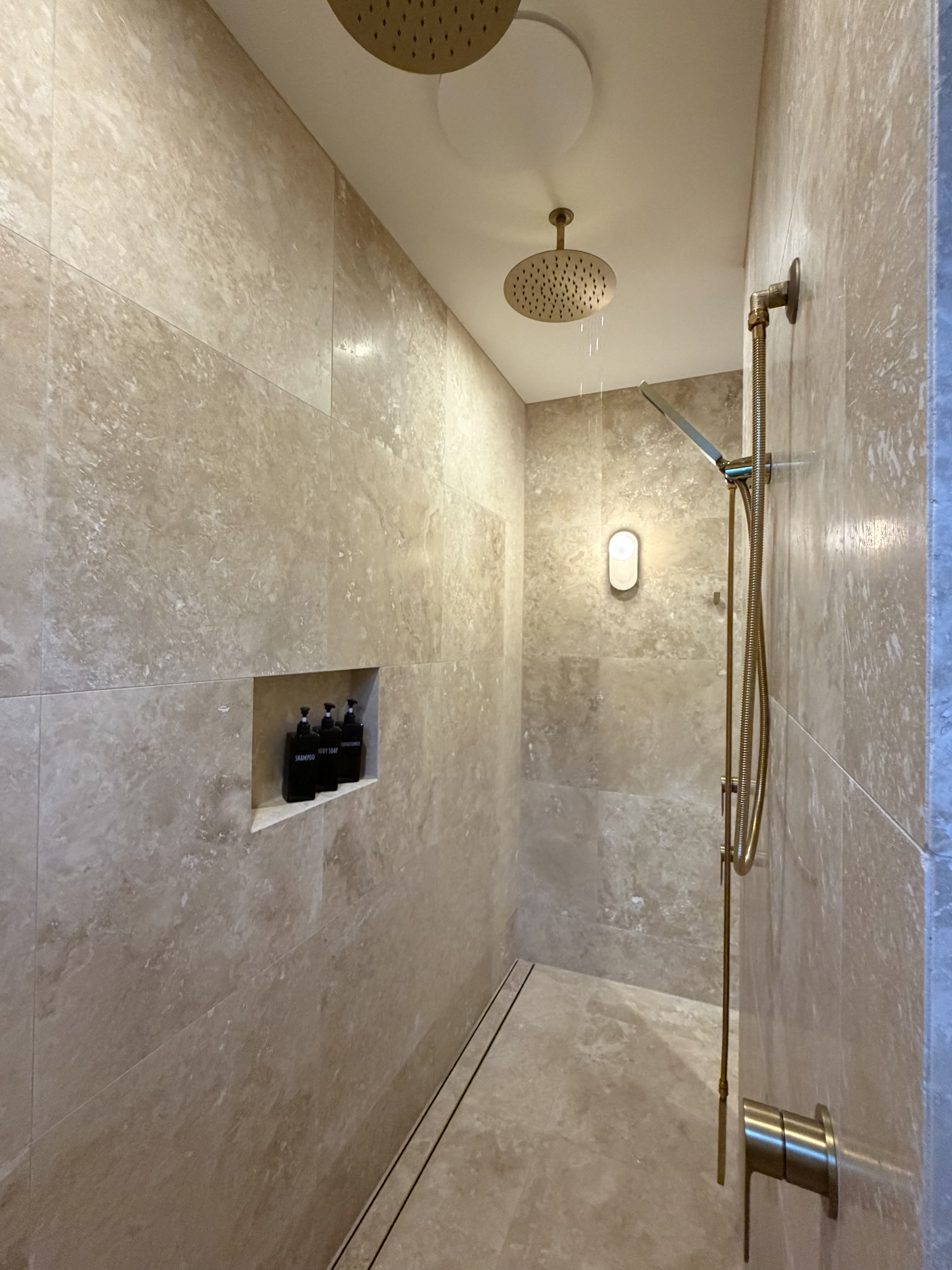 Completed travertine double shower with niche and brass fixtures